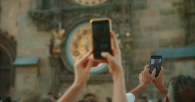 Antik bir Avrupa binasında tarihi bir Prag Astronomik Saatini yakalayan akıllı telefonları tutan eller kalabalık bir turistik bölgede karmaşık altın detaylara sahip..