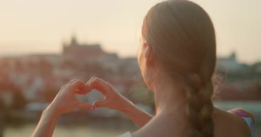Gün batımında Prag siluetini çerçeveletip şehir için bir aşk sembolü olarak gösteren bir kalp şekli oluşturan bir kadın..