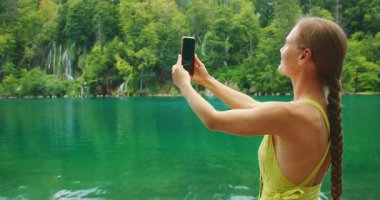 Plitvice Gölleri 'ndeki yaz ziyaretinde kadın zümrüt sularının ve şelalelerin yanında selfie çekiyor..