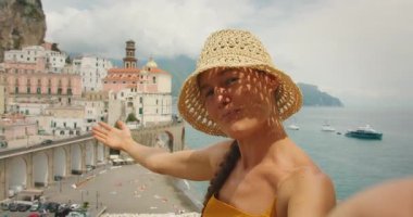 Gülümseyen kadın sosyal medya için selfie çeken Amalfi Coast kasabasını işaret ediyor.