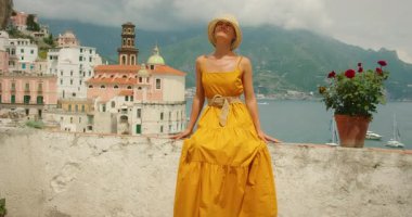 İtalya, Atrani 'de teras duvarında oturan bir kadın. Arka planda tekneler ve binalar var..