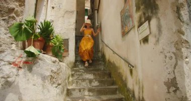 Sarı elbiseli kadın, eski bir Avrupa köyünde dar taş basamaklardan iniyor..