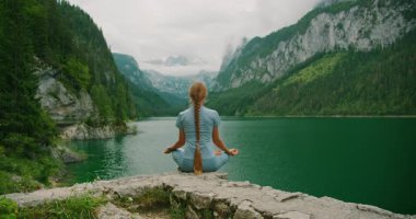 Bir kadın, bereketli ormanlar ve Avusturya yazında dramatik dağ manzaralarıyla çevrili, kristal berraklığında Gosau Gölü 'nde meditasyon yapıyor..