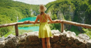 Hırvatistan 'daki Plitvice Gölleri Ulusal Parkı' ndaki kayalık bir bakış açısından canlı mavi suya ve şelaleye bakan kadın.
