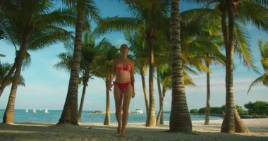 Uzun palmiye ağaçları ve mavi gökyüzü ile kaplı kumlu tropikal plajda yürüyen mutlu kadın..