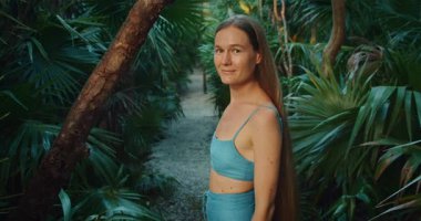 Kadın orman yolunda yürüyor. Palmiye ağaçlarının yemyeşil yeşiliyle çevrili..