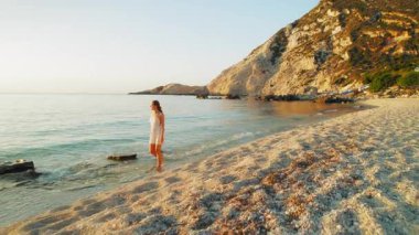 Yaz turu sırasında Yunanistan 'ın Kefalonia kentindeki kayalık kayalıkların yakınında gün batımında sahilde yürüyen bir kadın.
