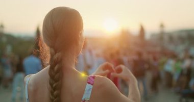 Prag 'da sıcak akşam saatlerinde kalabalığın üzerinde elleri günbatımına doğru kalp şeklini alan kadın..