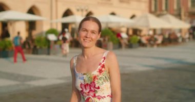 Giyinik bir kadın Avrupa meydanında kameraya gülümsüyor. Günün altın saatinde..