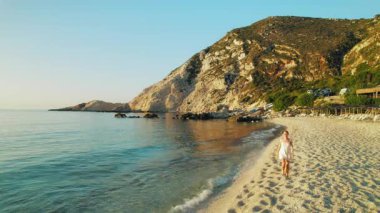 Kefalonia 'da sakin bir kumsalda, sıcak akşam ışığında çıplak ayakla yürüyen bir kadın..