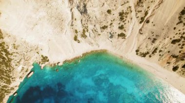 Yunanistan 'da kayalık kayalıklarla çevrili turkuaz körfez ve kumlu plajın aşağı manzarası.
