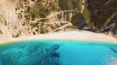 Sarp kayalıklardan Kefalonya 'daki Myrtos beyaz plajına uzanan virajlı bir yol..
