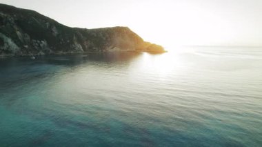 Yunanistan 'ın Sefalonya kentindeki engebeli kıyı şeridi yakınlarındaki sakin İyon Denizi üzerinde altın gün batımı yansıyor.