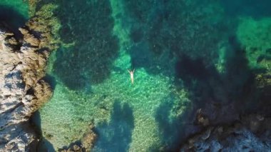 Yaz tatillerinde Kefalonia 'da kayalık bir koyda yüzen yalnız yüzücü kadın..