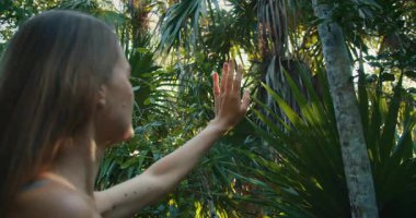 Yumuşak güneş ışığı altında tropikal bir ormanda yapraklara uzanan bir kadın..