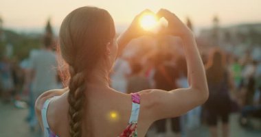 Kadın, elleri batan güneşin etrafında turistlerle çevrili tarihi bir Avrupa köprüsünde bir kalp şekli oluşturuyor..