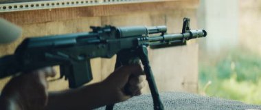 Atış talimi sırasında mermi kovanı olarak bipod destekli tüfeği ateşleyen adam..