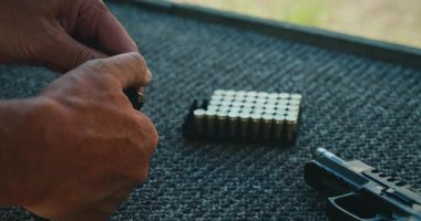 Atış poligonunda, halı döşeli bankta, tabancanın yanında şarjör hazırlayan adam..