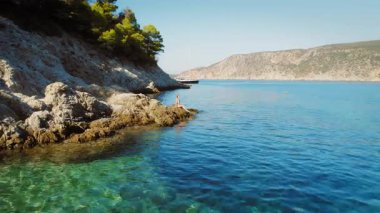 Güneşli bir günde Kefalonia 'da çamlık ormanı yakınlarındaki kayalıklarda oturan bir kadın..