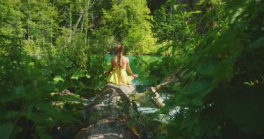 Kadın, Plitvice Orman Parkı 'ndaki göle giden akarsuyun üzerinde meditasyon yapıyor..