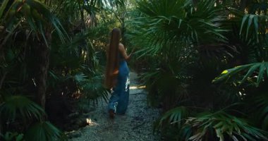 Tropikal orman yolunda çıplak ayakla yürüyen uzun saçlı bir kadın..