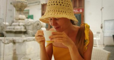 Hasır şapkalı gülümseyen kadın Amalfi İtalya 'da bir çeşmenin yanındaki açık bir kafede kahve içiyor..