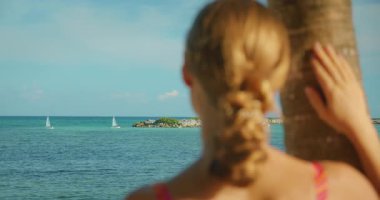 Meksika 'da bir palmiye ağacında elini dinlendirirken kadın turkuaz denize bakar..