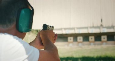 Kulak koruyucusu olan yaşlı bir adam atış menziline nişan alıyor..