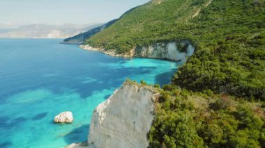 Uçurumun kenarında duran çift turkuvaz suyu yemyeşil ağaçlar ve arka planda dramatik kayalık kıyı şeridi..