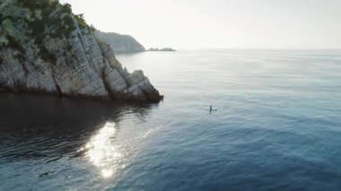 Yalnız kaykaycı, sakin İyon sularında engebeli kireçtaşı kayalıklarının yanından süzülüyor..