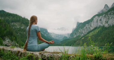 Kadın Avusturya 'daki Gosau Gölü' nde meditasyon yapıyor, yemyeşil dağlar ve sisli gökyüzü ile çevrili..