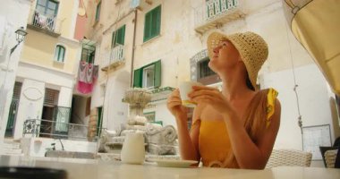Güneşli Amalfi kafe meydanında şapkalı, cappuccino içen bir kadın..