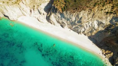 Zümrüt deniz suları ve kayalık uçurumlarla el değmemiş beyaz kumsal manzarası.