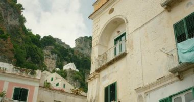 Atrani kasabasındaki kayalık uçurumlar ve pastel binalarla tepe manzaralı evler ve yeşillikler..