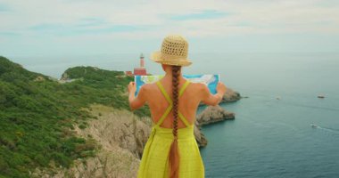 Haritalı bir turist, Capri Punta Carena deniz fenerinin etrafındaki manzaraya bakıyor..