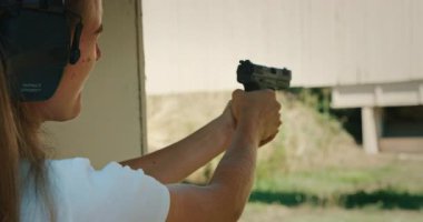 Odaklanmış bir kadın antrenman sırasında atış poligonuna silah doğrultup ateş ediyor..