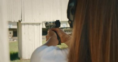 İşitme korumalı bir kadın silah doğrultuyor ve dışarıdaki hedeflere ateş ediyor..