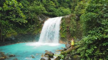 Kosta Rika 'nın yoğun yağmur ormanlarında turkuaz şelale havuzu kenarında duran kadın.
