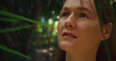 Yeşil yemyeşil, yemyeşil tropikal orman ortamında bir kadın korkuyla yukarıya bakıyor..