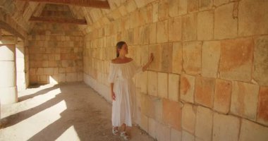 Beyaz elbiseli kadın Uxmal harabelerinin içindeki antik taş duvara dokunuyor, Meksika.