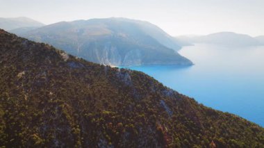 Yunanistan 'ın Kefalonia adasındaki gizli bir sahili çevreleyen orman tepeleri ve berrak mavi sular.