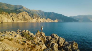 Kefalonia 'da gün batımında deniz kenarındaki kayalık kayalıklarda duran kadın Yunanistan.