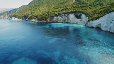 Turkuaz sular Kefalonya 'daki beyaz kireçtaşı kayalıkları ve yeşil tepelere çarpıyor.
