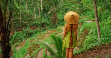 Yürüyüş turu sırasında Tegallalang Bali 'de pirinç tarlalarını izleyen geleneksel şapkalı bir gezgin..