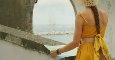 İtalya 'nın kıyı köyünde elinde haritayla okyanusa bakan kadının arka görüntüsü..