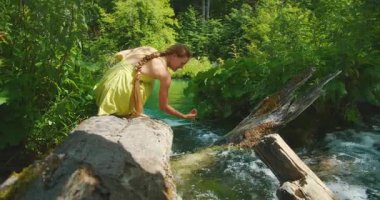 Plitvice Lakes Ulusal Parkı 'ndaki bir ağaç gövdesinden sarkan kadın suya dokunuyor..