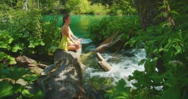 Plitvice Lakes Ulusal Parkı 'ndaki şelale deresinin yakınındaki bir kütükte meditasyon yapan kadın..