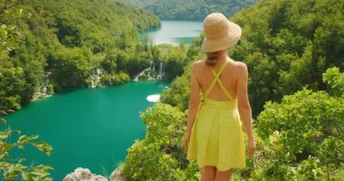 Plitvice Gölleri 'nde yaz mevsiminde turkuaz göl ve şelalelere bakan elbiseli bir kadın..