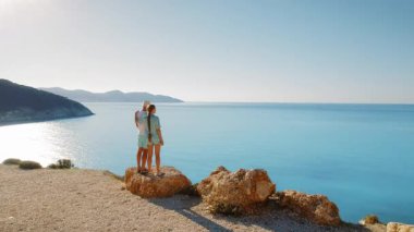 Çift kayalık çıkıntıda durup sonsuz mavi denizi manzaralı uçurum manzarasına bakar..