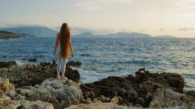 Kadın kayalık sahilde duruyor ve Cephalonia 'da rüzgarlı açık okyanusa bakıyor..
